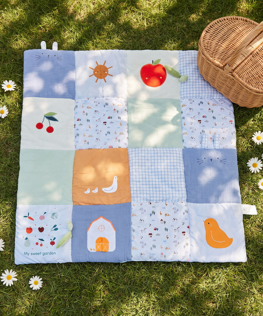 The Nurtory quilted play mat laid out on grass beside a picnic basket